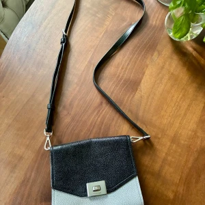 Michael Kors Cassie handväska  - Svart och grå Michael Kors axelremsväska, modell Cassie, med justerbar rem och silverfärgade detaljer. Väskan har fack inuti. Väldigt bra skick.  Ca 17 x 14 cm. Kan skickas eller hämtas hos mig på Kungsholmstorg.