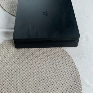PlayStation 4 Slim - Sony PlayStation 4 Slim i svart. Konsolen är i gott skick med mindre ytliga repor, inga synliga större skador. Perfekt för gaming med två USB-portar framtill och HDMI, LAN och strömanslutning baktill. En pålitlig spelkonsol för både nya och erfarna spelare. Säljer billigt för har köpt ps5 använt detta ung 7 år men funkar galant lite sega menyer och går lika snabbt längre såklart 