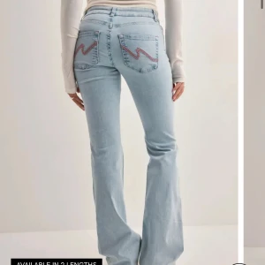 Ljusblå bootcut jeans från Nelly - Säljer ett par ljusblå bootcut jeans från Nelly med snygga röda och vita broderade detaljer på bakfickorna. Jeansen har normal midja, klassisk femficksdesign och är tillverkade i mjuk bomullsdenim. Perfekta för dig som gillar en retroinspirerad look.    Aldrig använda med prislapp på. Ordinarie pris: 699kr