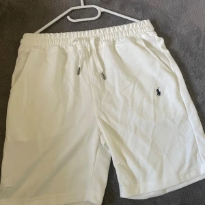 Vita shorts från Polo Ralph Lauren - Snygga vita shorts från Polo Ralph Lauren med elastisk midja och snörning framtill. Klassisk design med fickor på sidorna och den ikoniska Polo-loggan broderad på vänster ben. Perfekta för chill dagar och sommarhäng.