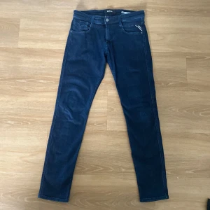 Replay Anbass jeans mörkblå 30/32 - Snygga mörkblå Replay Anbass jeans i slim fit med klassisk femficksdesign och dragkedja. Jeansen har raka ben och är tillverkade i mjukt denimtyg som sitter skönt. Perfekta för dig som gillar stilrena och moderna jeans.
