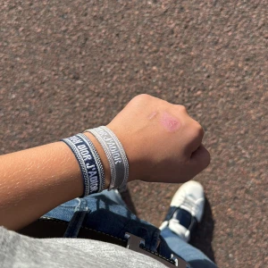 Christian Dior J'Adior armband blå - Säljer ett snyggt Christian Dior J'Adior armband i blått och vitt tyg med broderad logga och tofsar i ändarna. Armbandet har justerbar knytning och är perfekt för att ge din outfit en lyxig touch.