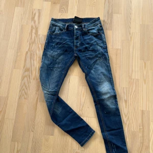 Mörkblå skinny jeans Kings Will Dream - Säljer ett par mörkblå skinny jeans från Kings Will Dream med coola slitningar och färgstänk. Jeansen har klassisk femficksdesign, smal passform och snygga kontrastsömmar. Perfekta för dig som gillar streetstyle och vill sticka ut.