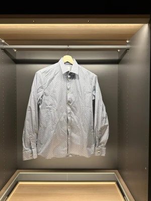 Mönstrad blå skjorta från Bläck - Snygg blå skjorta från Bläck med diskret mönster i vitt och mörkblått. Skjortan har klassisk krage, långa ärmar och knappar framtill. Skräddarsydd passform som sitter riktigt bra och känns modern. Perfekt för dig som vill ha en stilren men ändå unik look.