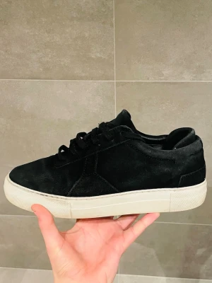 Arigato Mocca skor - Stilrena svarta sneakers i mocka med tjock vit platt sula. Skorna har klassisk snörning och en enkel, clean design som passar till det mesta. Perfekta för dig som gillar en minimalistisk look med lite extra känsla tack vare mockamaterialet.