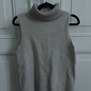 Grå ärmlös stickad polotopp - Stilren grå ärmlös stickad topp med hög polokrage. I fint skick. 
