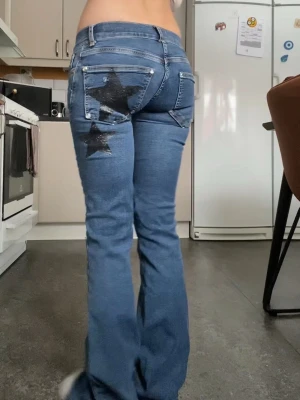 Blå jeans med svarta stjärnor - Säljer ett par blå jeans med bootcut-modell och snygga svarta glitterstjärnor på bakfickan och benet. Från mitt uf : truestarjeans , lågmidjade och utsvängda, måtten: ytterben: 97cm innerben:81 lårlängd: 16cm rakt över