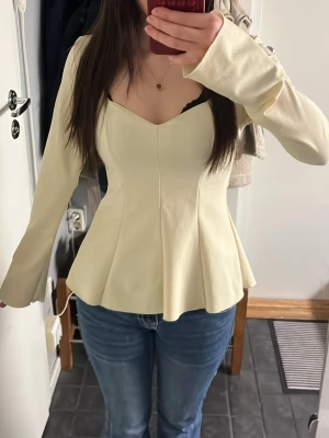Gina Tricot - Supersnygg ljusgul blus från Gina young 14+ med v-ringad hals och figurnära passform som markerar midjan. Blusen har långa ärmar och en lätt utsvängd nederdel. Storlek S❣️