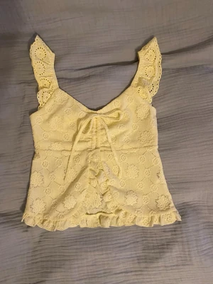 Gul spetsig linnetopp med volang - Har aldrig använts. Supersöt gul linnetopp med blommor, volangkant och spetsdetaljer. Super somrig och fin. skriv om ni undrar om något 💕
