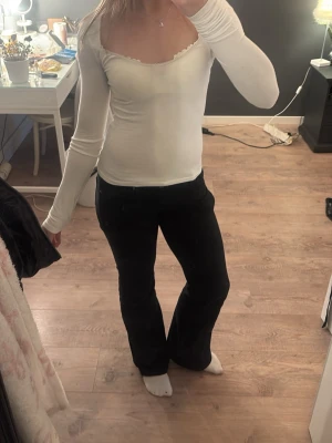 Vit långärmad topp med spetskant - Säljer en vit långärmad topp med söt spetskant runt den breda, v-ringade urringningen. Toppen är tight i passformen och gjord i ett mjukt, stretchigt material som känns skönt mot huden. Perfekt att styla med jeans eller kjol för en clean look.