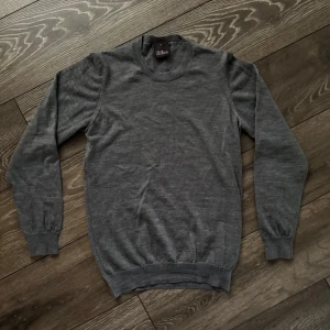 Grå stickad tröja från Oscar Jacobson - Säljer en stilren grå stickad tröja från Oscar Jacobson i storlek S. Tröjan har rund halsringning, ribbade muddar och är tillverkad i mjuk ull. Perfekt för lager på lager under kyliga dagar.