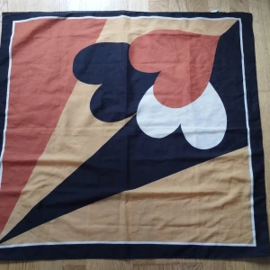 Scarf i jordnära färger med hjärtmönster - Stor fyrkantig halsduk i med fint grafiskt hjärtmönster i svart, beige, vit och rödorange. Färgerna passar till många ytterplagg, skor och väskor vilket ger en harmonisk stylad look. Snygg retrostil som sticker ut och passar perfekt att knyta runt halsen, väskan eller i håret. Tillverkad i Italien.