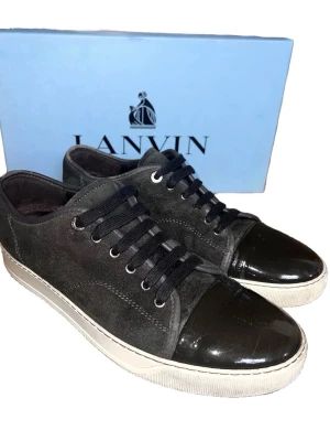 Mörkblå mockasneakers från Lanvin - Snygga sneakers från Lanvin i mörkblå mocka med lackad tå och vita sulor. Skorna har svarta snören och en klassisk låg profil. Perfekta för dig som gillar stilrena detaljer och exklusiva material. box ingår ej
