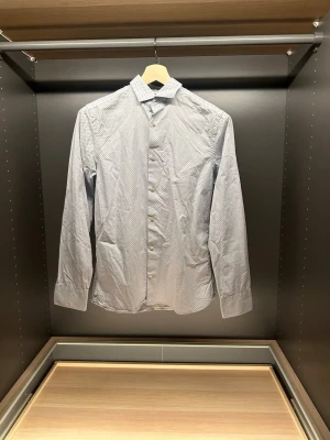 Ljusblå skjorta The Tailoring Club - Säljer en ljusblå skjorta från The Tailoring Club i premium bomull. Skjortan har ett diskret prickigt mönster, klassisk krage och knappar framtill. Långärmad modell som passar perfekt till jeans eller chinos.