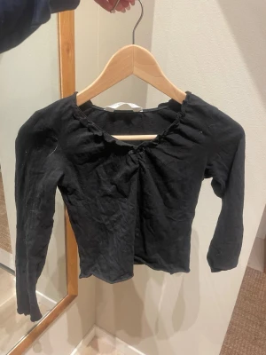 Svart långärmad topp från H&M - En svart långärmad topp från H&M med rundad halsringning och liten rosett framtill. Modellen är enkel och tight, perfekt att styla med jeans eller kjol. Tillverkad i mjukt bomullstyg som känns skönt mot huden. Skriv vid eventuella frågor