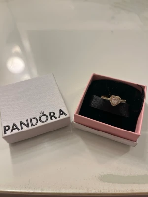 Guldig pandora ring - Bilderna visar en guldfärgad ring från Pandora med hjärtformad sten