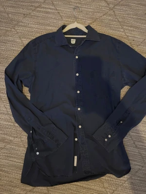  Jacob Cohen skjorta - Säljer en mörkblå skjorta från Jacob Cohen, handgjord i Veneto, Italien. Skjortan är i 100% bomull, har klassisk krage, vita knappar och en bröstficka. Perfekt för dig som gillar stilrena och exklusiva plagg.