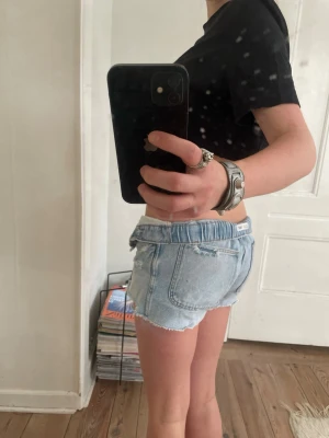 Lågmidjade ljusblå jeansshorts - Säljer ett par lågmidjade ljusblå jeansshorts från SIXTH JUNE. De har råa, fransiga kanter och slitna detaljer för en avslappnad vibe. Klassisk femficksmodell med knappgylf och silverfärgade nitar. Perfekta till sommaren!