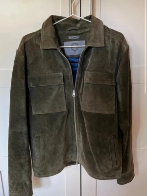 Olivgrön mockajacka Human Scales M - Säljer en tvärfet olivgrön mockajacka från Human Scales i storlek M. Säljer då den är lite för liten. Nypris ca 3000kr