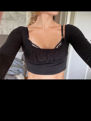 Svart croppad långärmad topp - Säljer en svart croppad topp med långa ärmar och rynkade detaljer vid bysten. Toppen har en tight passform och är tillverkad i ett mjukt bomullsmaterial. Perfekt att styla med höga jeans eller kjol.