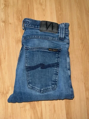 Nudie Jeans  - Säljer ett par jeans från Nudie Jeans men snygg blå tvätt. Midja 33cm, längd 110cm. OBS Jeansen har ett litet hål baktill- se bild 6. JAG SKICKAR EJ FLER BILDER NÄR JAG BÄR JEANSEN! för bättre inblick i passformen rekommenderar jag att googla på modellnamnet. För storleksguide kolla måtten noggrant då jeansen alltid kan vara uppsydda heller krympta och jag ej tar emot returer :) s6,1