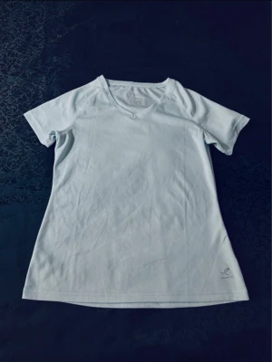 Ljusblå tränings-tshirt Energetics - Sportig ljusblå t-shirt från Energetics med v-ringning och korta ärmar. Tillverkad i ett lätt och ventilerande polyestermaterial som passar perfekt till träning. Enkel och clean design utan mönster, med liten logga nere vid fållen.