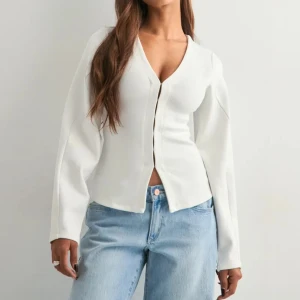 Nelly - Waist focus cardigan - Figursydd kofta med intagna midja från Nelly i färgen vit. Koftan sitter jättefint på kroppen men är lite stor i ärmarna för mig! Brukar använda xs/s! Har inte använts mer en gång!