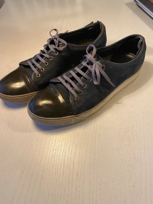 Lanvin mörkblå sneakers med skinn - Snygga sneakers från Lanvin storlek 43 men är stora i storlek så passar absolut 44 också. Dom är i mörkblå mocka med svart skinn på tån och sidorna. Skorna har rund tå, platt sula och grå snörning. Yttersulan är vit och märkt med Lanvin. Perfekt för dig som gillar stilrena och exklusiva sneakers. Hör gärna av dig vid frågor. Priset är ej hugget i sten.
