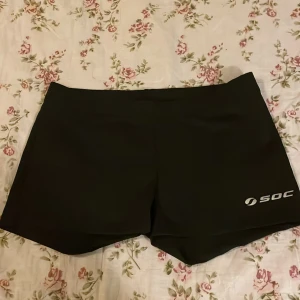 Svarta träningsshorts från SOC - Svarta träningsshorts från SOC med TCS Air-teknologi. De har en clean och tight passform, elastisk midja och är gjorda i ett syntetmaterial som andas. Perfekta för gymmet eller löprundan. Diskret logga på benet för en sportig vibe.