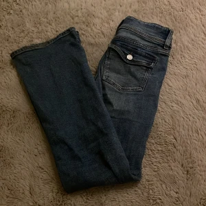 Blå bootcut jeans från Gina Tricot Young - Snygga blå jeans från Gina Tricot i bootcut-modell. Jeansen har klassiska fickor med lock och silverfärgade knappar bak, samt dubbla knappar fram. Jeansen är sköna och ör i storlek 158 men passar även mig som ör 163 perfekt. Jag säljer på grund av att de ej kommer till användning. Ändarna är lite slitna och smutsiga som man kan se på bild men det är inget som riktigt syns eller tänkes på. Skriv för fler bilder!