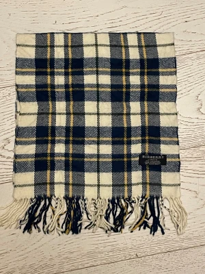 Rutig kashmirhalsduk från Burberry - Snygg halsduk från Burberry i 100% kashmir med klassiskt rutigt mönster i marinblått, vitt och inslag av gult. Mjukt material och fransar i ändarna. Perfekt accessoar för att lyfta din vinterstil med lyxig känsla och tidlös design.