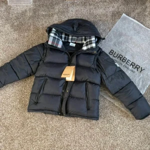 Svart pufferjacka från Burberry - Säljer en svart pufferjacka från Burberry med stor patch på ärmen där det står 'BURBERRY LONDON ENGLAND'. Jackan har huva med snörning, dragkedja och knappar framtill samt fickor med dragkedja. Insidan av huvan har rutigt mönster i svart och vitt.