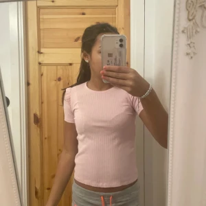 Rosa ribbad topp från Zara - Säljer en ljusrosa ribbad topp från Zara med korta ärmar och små volangdetaljer vid axlarna. Toppen är figurnära och har rund halsringning. Perfekt för dig som gillar en söt och enkel stil.