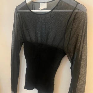 Svart mesh topp från H&M - Säljer en svart mesh topp från H&M i storlek S. Toppen har långärmade transparenta meshpartier och en ribbad, tight kropp med snygga detaljer över bysten. Perfekt för dig som gillar trendiga och edgy looks.