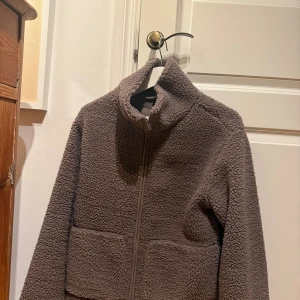 Brun teddyjacka från 157, storlek S - Mysig brun teddyjacka från 157 i storlek S. Jackan har hög krage, två stora fickor framtill och dragkedja hela vägen upp.  Fleece-liknande material 