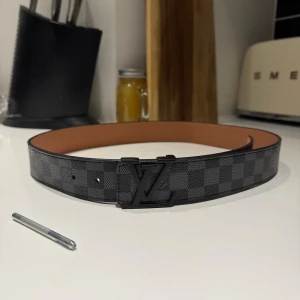 L-V svart rutigt skärp - Säljer ett L-V bälte med klassiskt svart rutigt mönster och stor L-V -logga i mattsvart metall. Bältet är tillverkat i skinn med beige insida. Skriv vid minsta intresse!