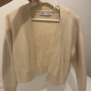 Beige ribbad kofta från Zara - Säljer en beige ribbad kofta från Zara i storlek S. Koftan har en öppen front utan knappar, långärmad design och är tillverkad i ett mjukt stickat material. Perfekt för lager-på-lager och chill stil. Passar dig som gillar neutrala färger och enkel look.