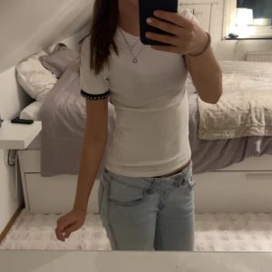 Vit t-shirt med pärldetaljer från Zara - Vit t-shirt från Zara, med korta ärmar och svart spetskant med pärlor vid ärmsluten. Jättesnygg men kommer ej till användning. 