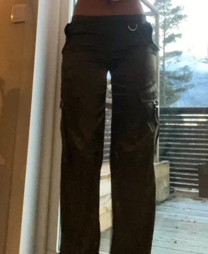 Olivgröna cargopants i silke - Snygga olivgröna cargopants från HM med glansig finish från silken. Byxorna har flera fickor, D-ringar och en elastisk midja med knapp. Rak passform och coola detaljer på benen som ger en streetig vibe. XXS men passar XS och S jättebra.