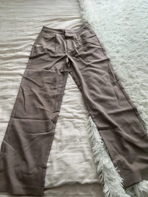 Beige wide kostymbyxor från 157 XS.  - Snygga beige kostymbyxor från 157 i storlek XS. Byxorna har ett wide fit med raka ben och klassisk midja. Perfekt för dig som gillar en clean och stilren look. Materialet känns mjukt och har en lätt struktur, vilket gör dem sköna att bära hela dagen.