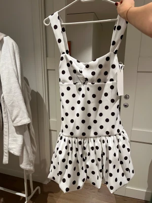 prickig klänning - Superfin vit kortklänning med svarta prickar och breda axelband. Klänningen har en volang nedtill som ger en lekfull vibe och är tillverkad i ett glansigt, mjukt polyestertyg. Perfekt för dig som gillar retro och statement-plagg. Efterfrågad och utsåld från zara!!!