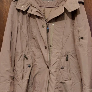 Beige parkajacka med dragkedja - Säljer en beige parkajacka med huva, flera fickor med dragkedja och knappar. Jackan har en klassisk design med hög krage och justerbara detaljer. Perfekt för kyliga dagar och har en snygg, neutral färg som passar till det mesta.