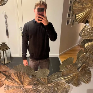 Svart Stone Island sweatshirt - Svart sweatshirt från Stone Island med klassisk rund hals och ikonisk patch på vänster ärm. Tröjan har ribbade muddar och är tillverkad i mjuk bomull. Perfekt för dig som gillar stilrena och snygga streetwear-plagg.