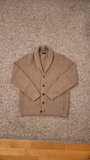 Beige stickad cardigan från Massimo Dutti - Säljer en beige, stickad cardigan från Massimo Dutti i storlek M (passar storlek L också) då den inte kommer till användning mer. Använd fåtal gånger och skicket är i princip som ny, inga slitningar eller defekter finns. Den har en snygg krage och fem knappar. Passar perfekt för dig som vill både hålla dig själv varm och stilig nu under vintern! Skick: 9/10