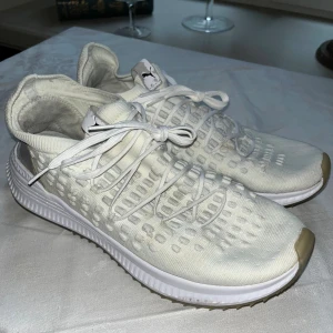 Puma sneakers vita - Säljer ett par vita Puma Ignite sneakers med stickad ovandel och cool struktur. Skorna har snörning, rund tå och en bekväm platt sula. Puma-logga på häl och plös. Perfekta för dig som gillar sportig och clean stil.