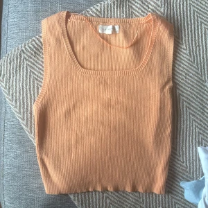 Ribbad orange linnetopp från LA Hearts - Säljer en snygg ribbad linnetopp från LA Hearts i en fräsch orange färg. Toppen är ärmlös med rundad halsringning och croppad passform, perfekt för varma dagar. Materialet är mjukt och stretchigt för en bekväm känsla.