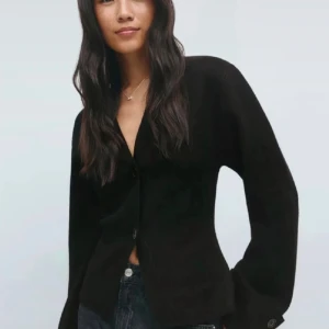 Svart kofta med knappar - Snygg svart kofta med långärmad design och knappar framtill. Koftan har en v-ringad öppning och är tillverkad i ett mjukt stickat material som ger en skön känsla. Perfekt att matcha med jeans för en stilren look.
