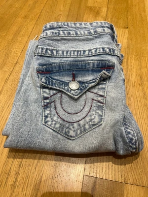 Ljusblåa bootcut true religion jeans 🩵 - Super snygga ljusblåa jeans från true religion i storlek 23 med röda detaljer på bak fickorna jeansen har hål på knäna och har en bootcut model och är mid rise🤗 köpte dom förra året på Nelly och seljer på grund av att de inte kommer till användning längre 🥰