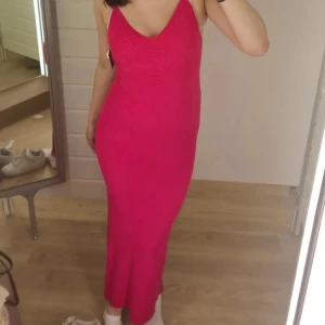 Rosa långklänning med smala axelband - Säljer en snygg rosa långklänning med smala axelband och v-ringning. Klänningen har en tight passform och är ribbad i materialet, vilket ger en modern och stilren look. Perfekt för dig som vill sticka ut med färg och enkel design.