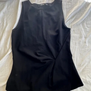 Svart ärmlös tröja från BikBok - En stilren svart tröja från BikBok i storlek S. Tröjan  är ärmlös med rund halsringning och har en figurnära passform. Tyget är slätt och känns mjukt, perfekt för dig som gillar minimalistisk och clean stil.